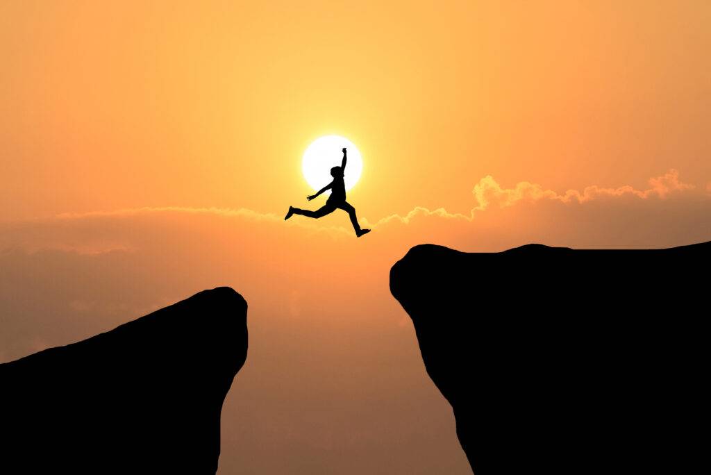 Les risques psychosociaux symbolisé par une silhouette d'homme sautant d'un roché à un autre sous le soleil couchant.
